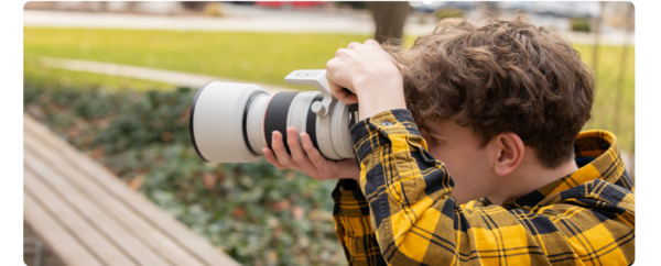 A student holds a camera and takes photos of something in the distance.