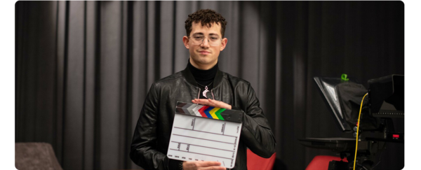 A student standing on a film set holding a clapper board.